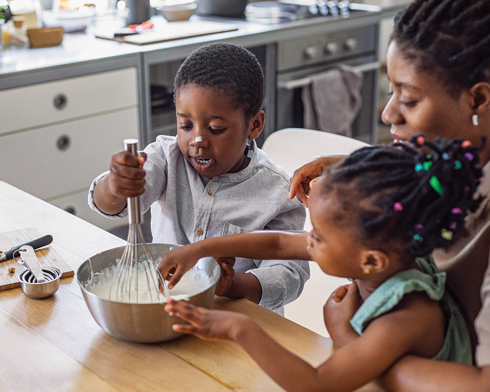 Child whisking ingredients with family in kitchen.