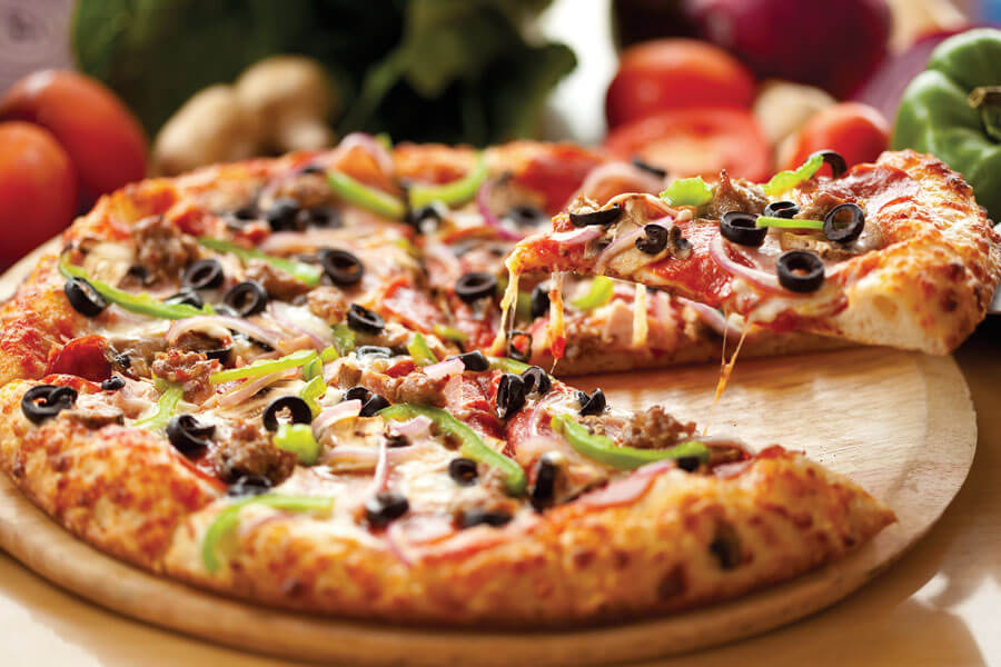 Slice of loaded pizza being lifted from tray.