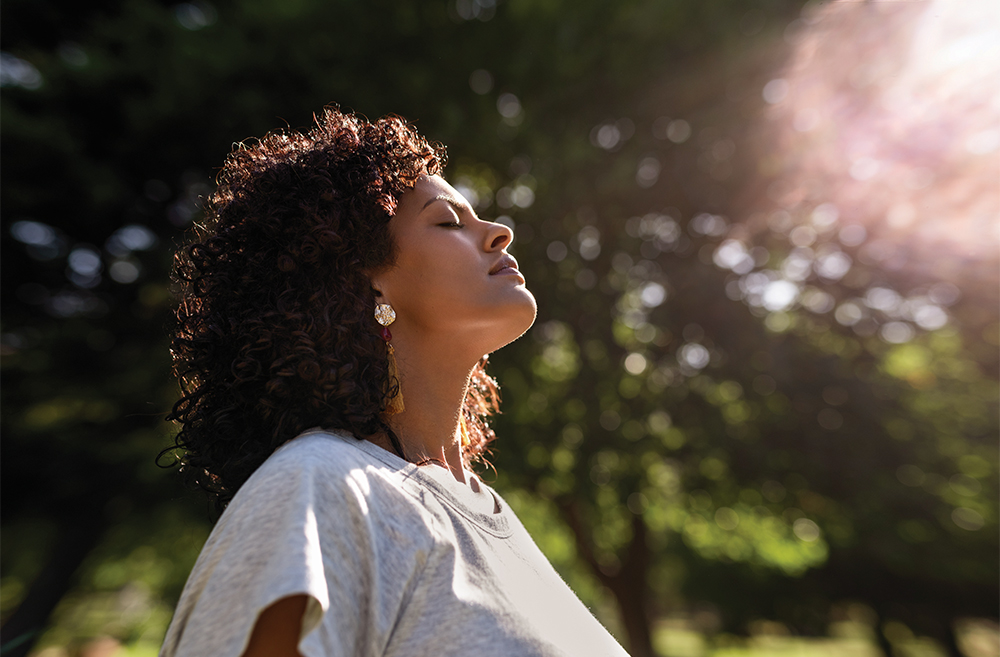 Woman enjoying sunlight with eyes closed in park.