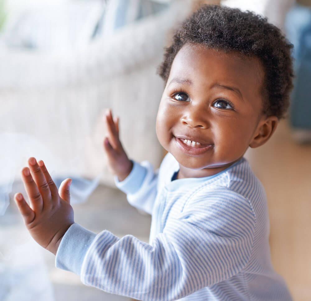 Smiling toddler touching glass, wearing striped shirt.