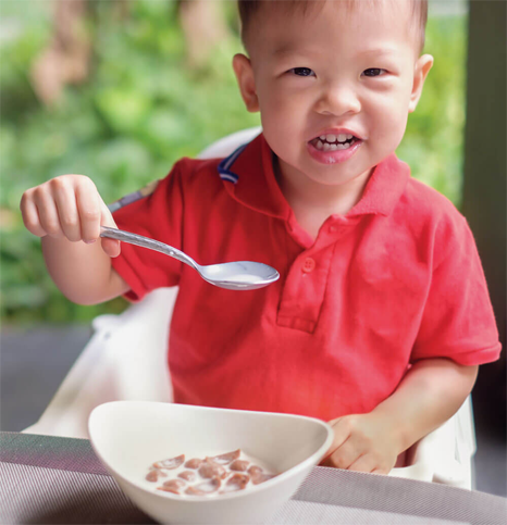 Child in red shirt eating cereal with spoon.
