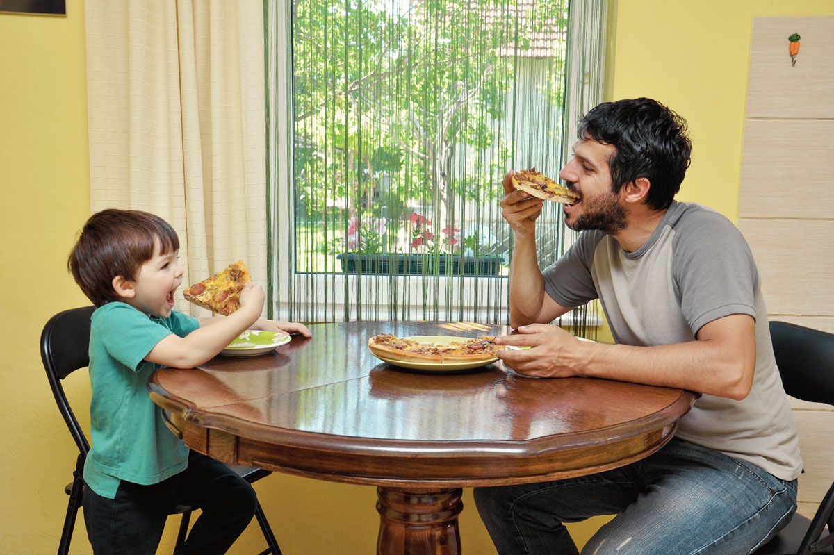 Father and son enjoying pizza at the table.