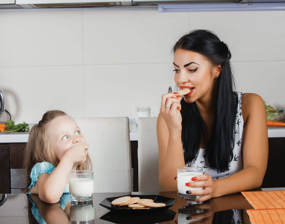 Woman and child enjoy cookies with milk together.