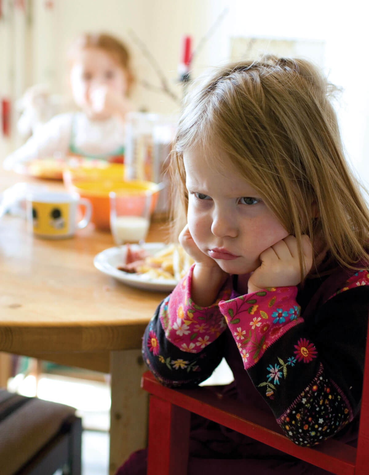 Child pouting at breakfast table, looking displeased.