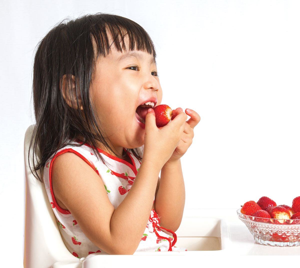Child happily eating fresh strawberries from bowl.