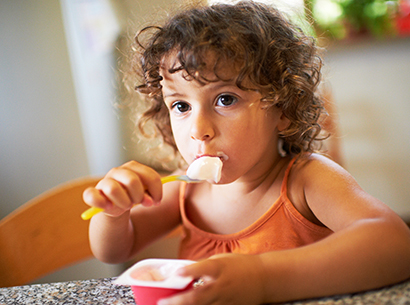 Child eating yogurt with a spoon.