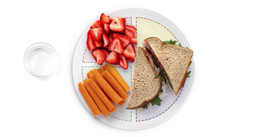 Sandwich, strawberries, and carrots on a sectioned plate.