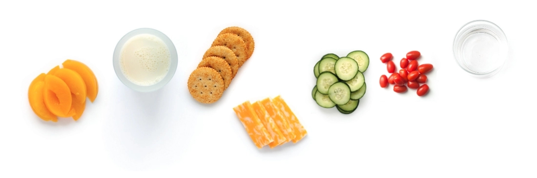 Sliced fruits, vegetables, crackers, and cheese on white background.