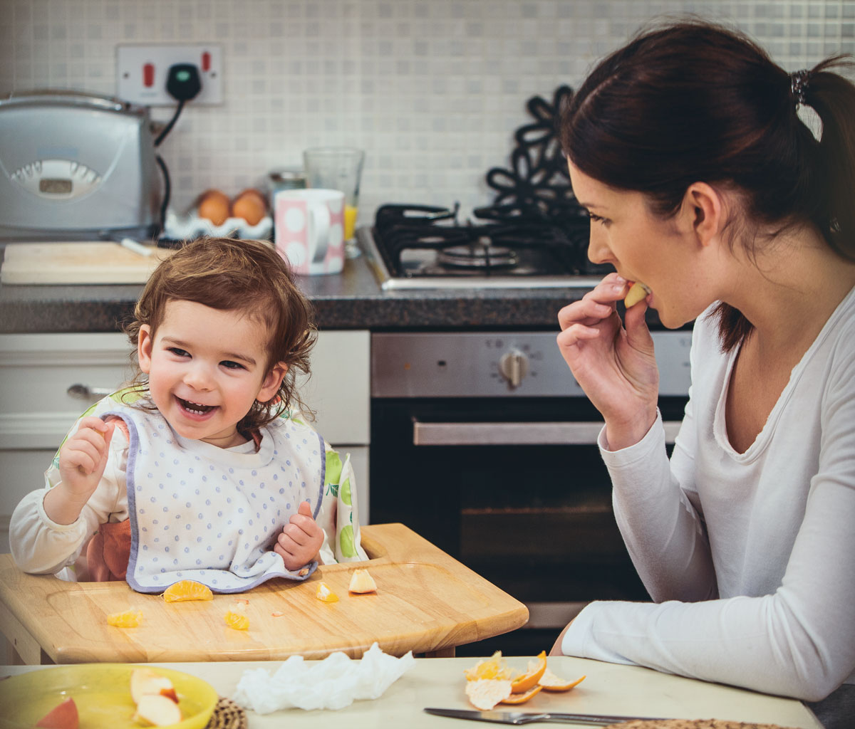Child and parent eating fruit in the kitchen.