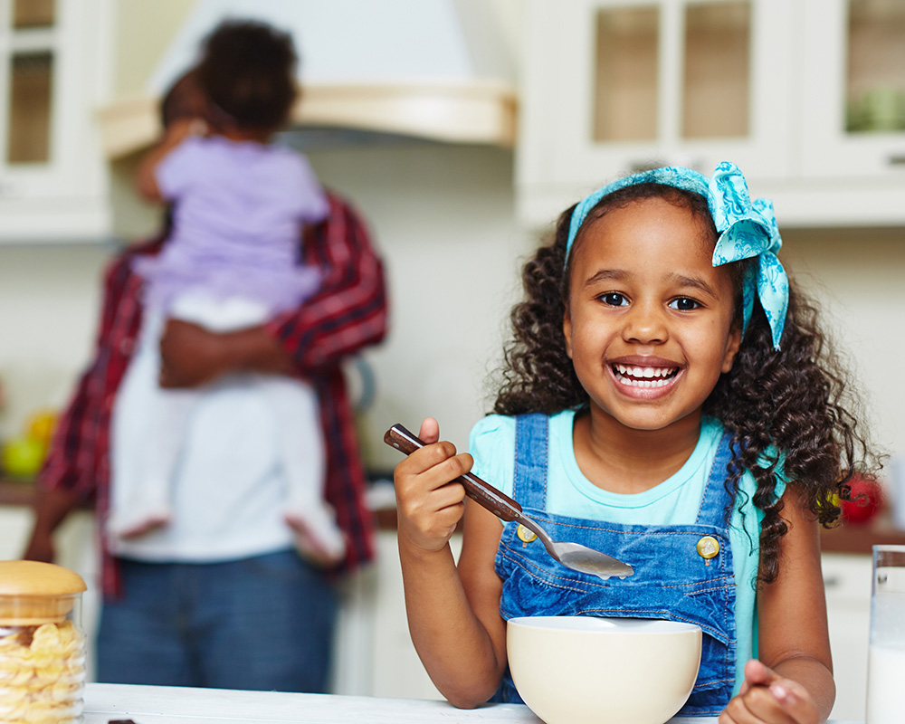 Smiling girl eating cereal in kitchen.