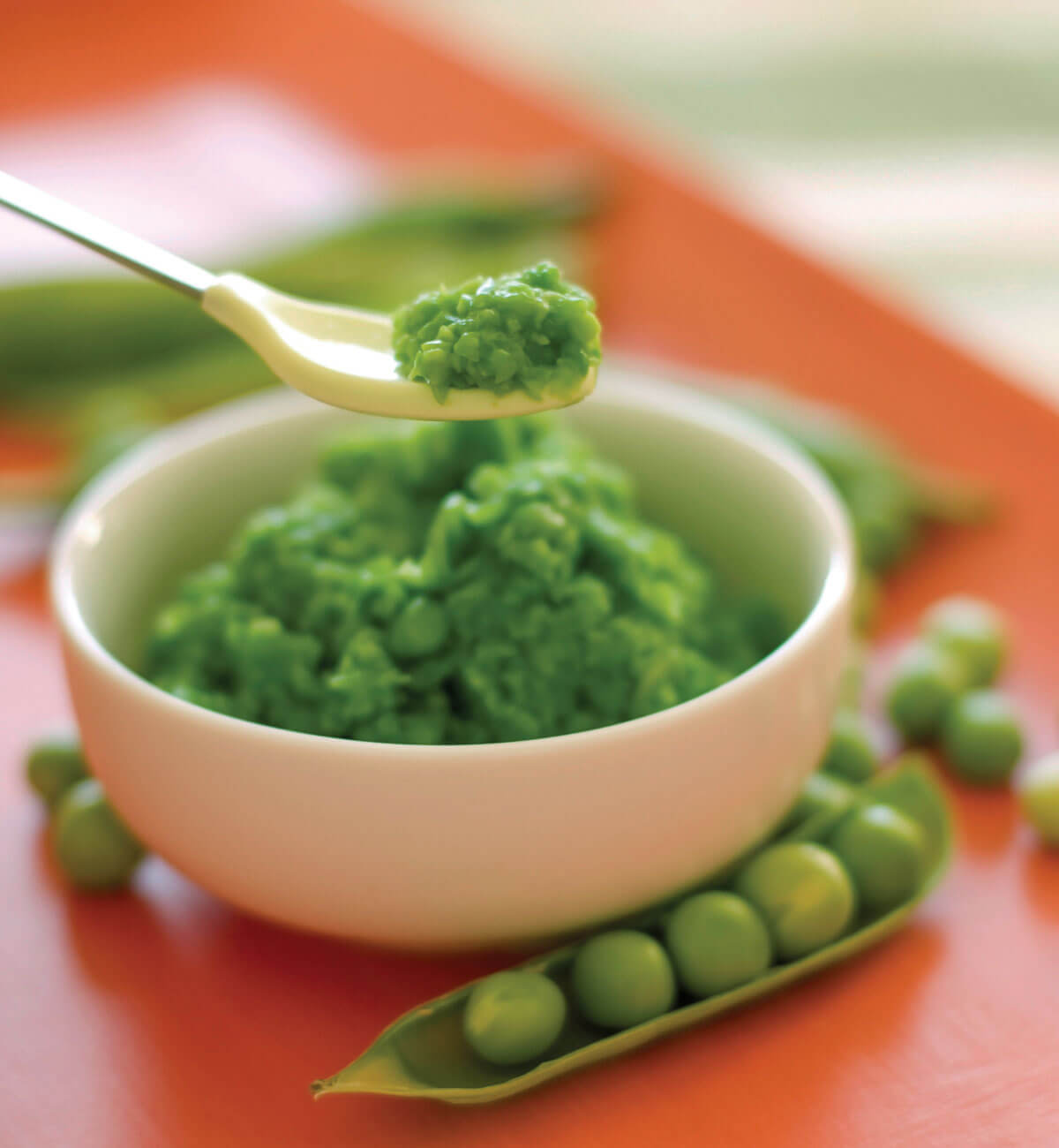 Spoonful of mashed peas above a bowl.