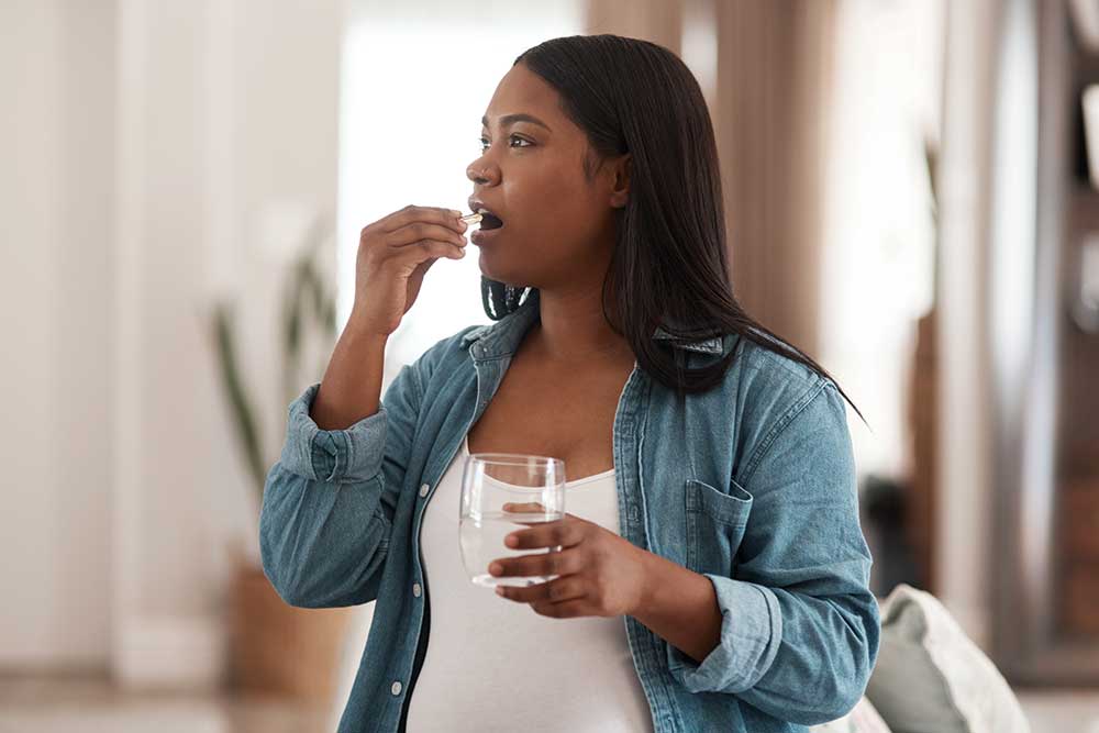 Woman taking a pill while holding a glass.