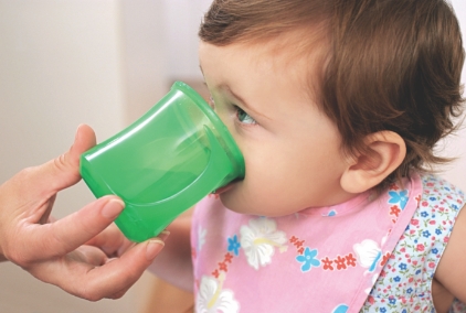 Child drinking from green cup, assisted by adult.