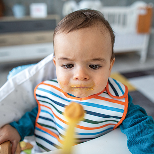 Baby in high chair examining spoonful of food.