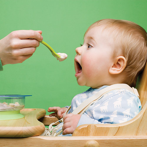 Baby being fed with a spoon, green background.