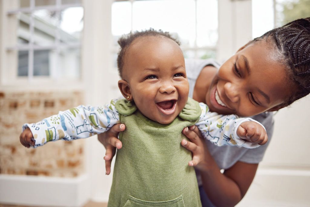 Smiling baby held by joyful woman indoors.