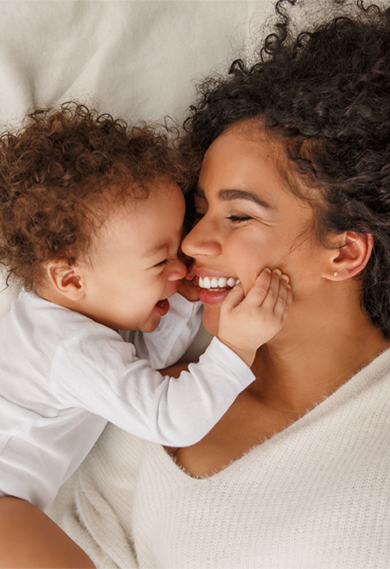 Mother and child smiling face-to-face on bed.