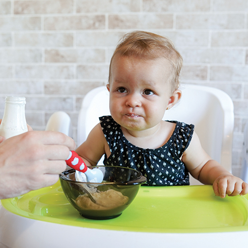 Baby eating from bowl with adult's help.