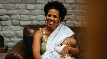 Smiling woman breastfeeding baby on couch.