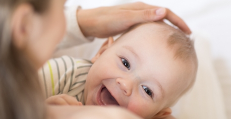 Baby smiling while being gently patted on head.