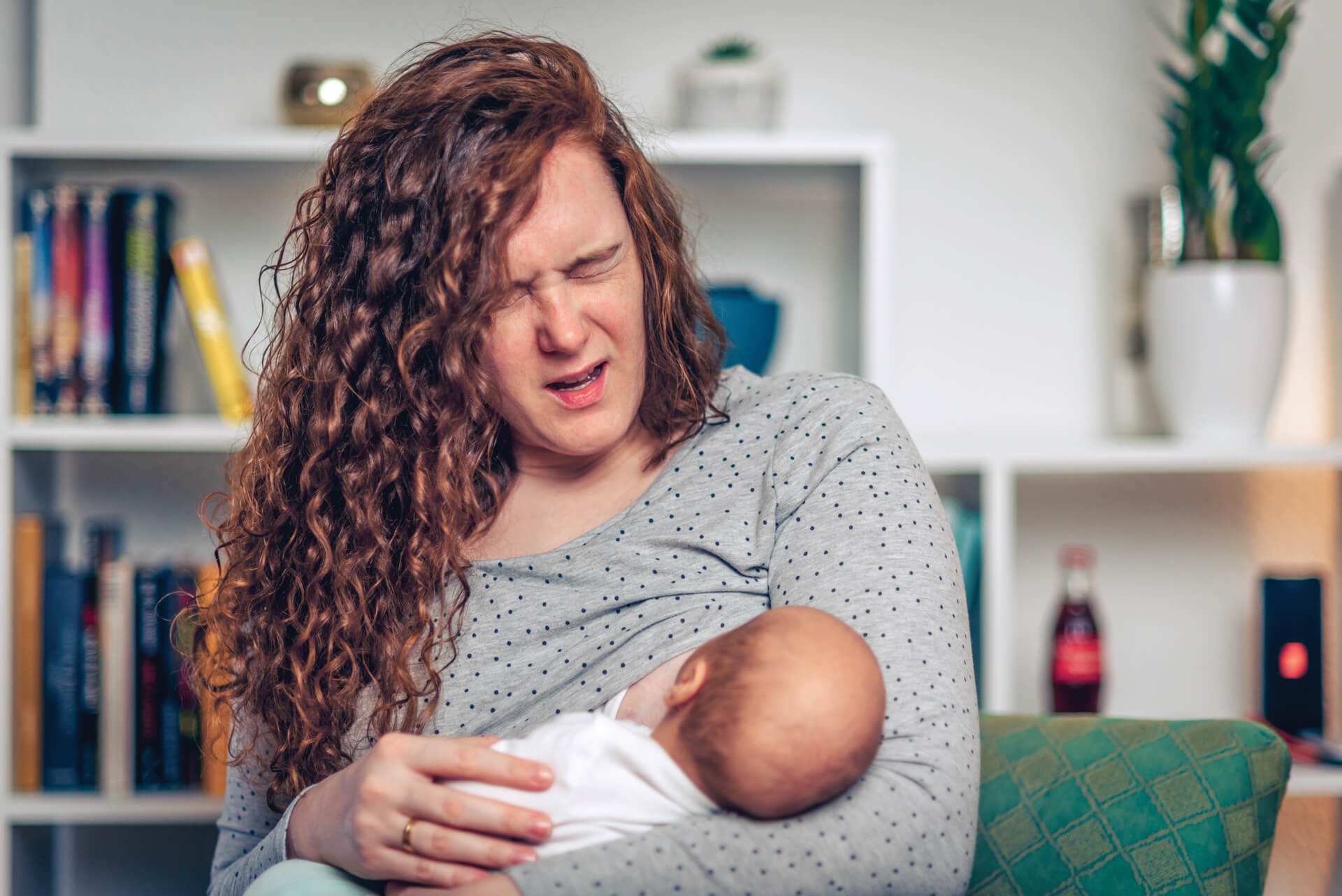 Mother breastfeeding baby, showing a pained expression.