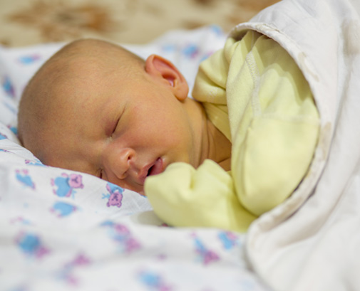 Newborn baby peacefully sleeping in yellow onesie.
