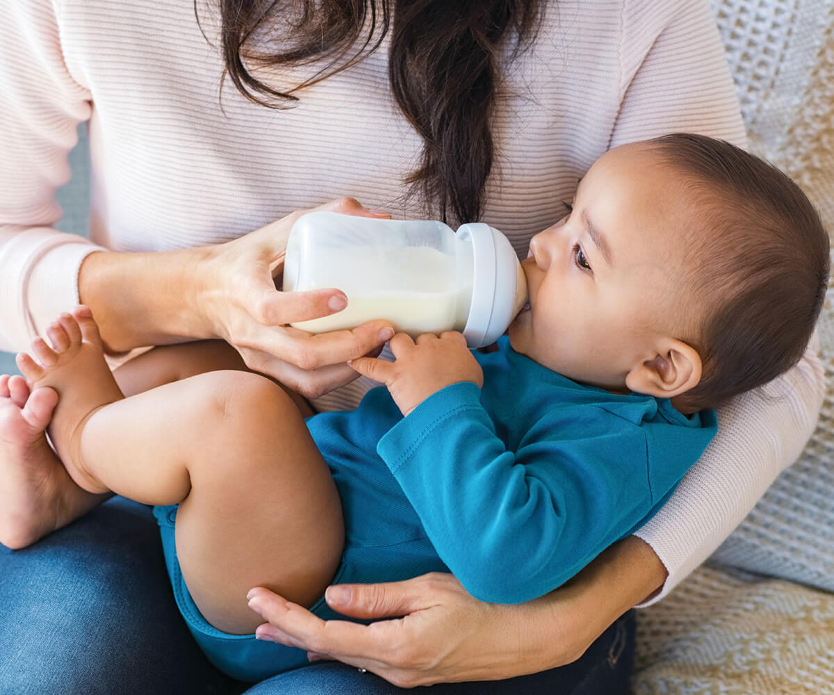 Baby drinking from bottle, held by caregiver.