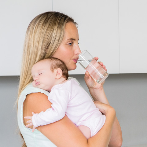 Mother holds sleeping baby while drinking water.