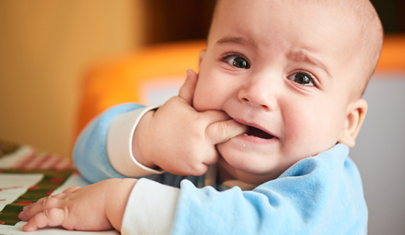 Baby chewing on fingers, wearing blue outfit.