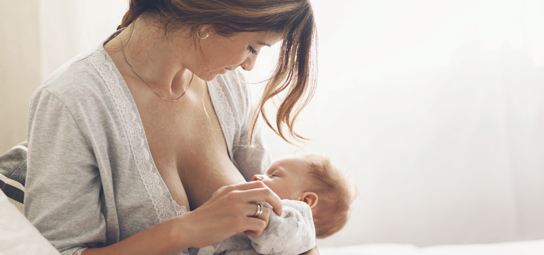 Mother breastfeeding her baby in a softly lit room, creating a warm and nurturing scene.