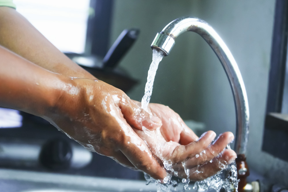 Hands washing under running water in kitchen sink.