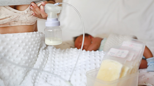 Breast pump collecting milk near sleeping baby.