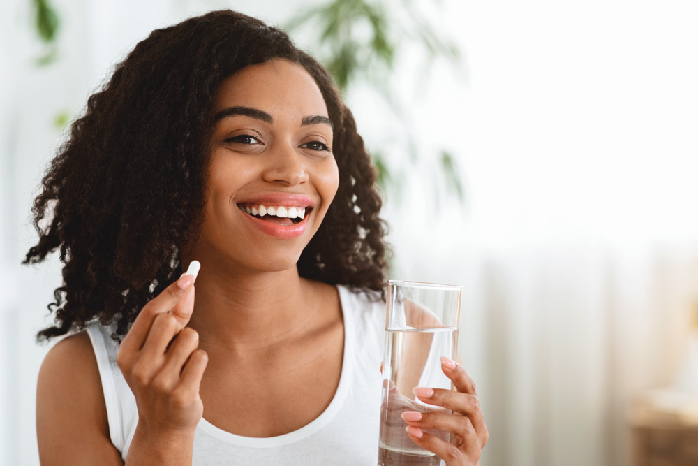 Smiling person holds pill and glass of water.