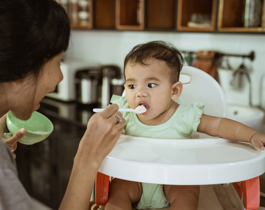 Adult feeding baby in high chair with spoon.