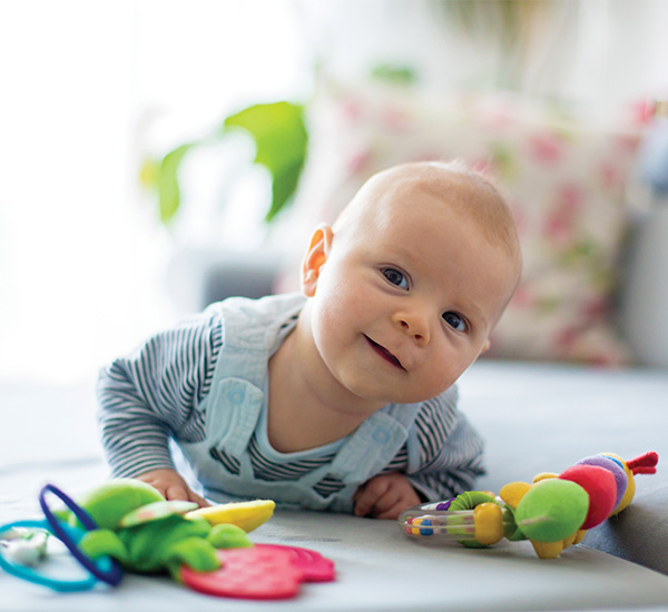 Baby in overalls, smiling while playing with toys.