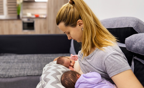 Mother breastfeeding twin infants on a couch.