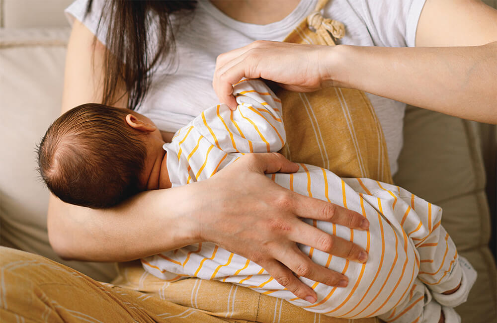 A mother breastfeeds her baby comfortably at home.