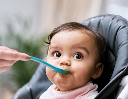 Baby eating with blue spoon in high chair.