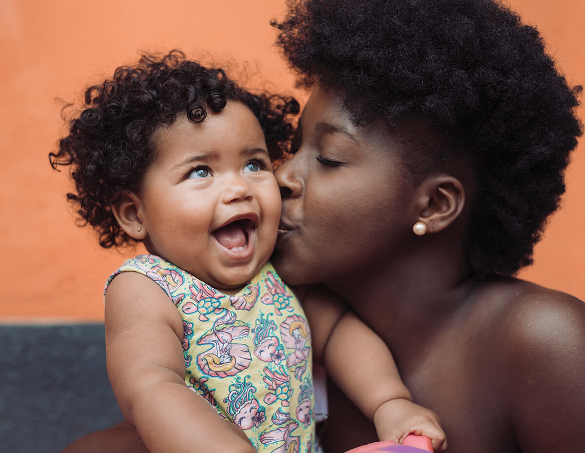 Mother kissing smiling baby against orange background.