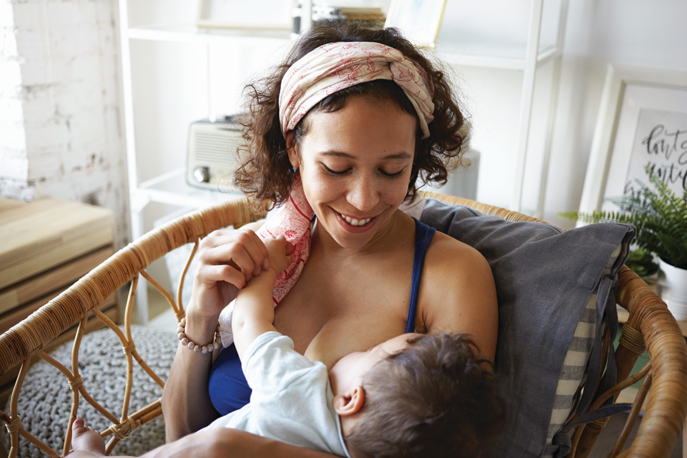 Mother breastfeeding baby in cozy chair, smiling gently.