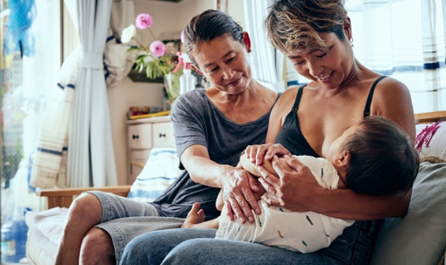 Two people smiling at nursing baby on sofa.