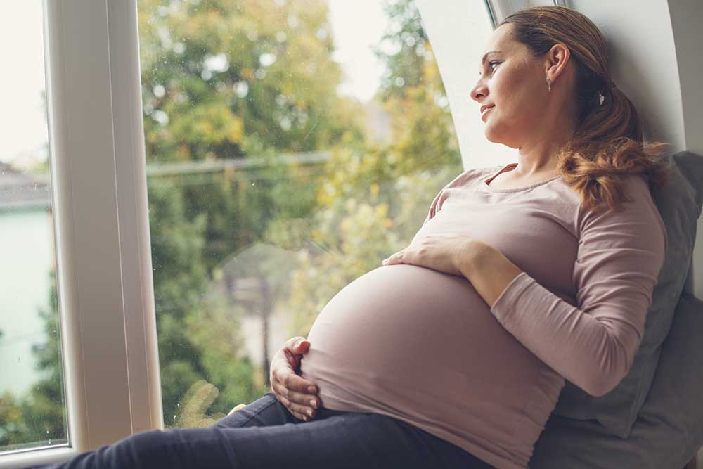 Pregnant woman relaxing, gazing out window thoughtfully.