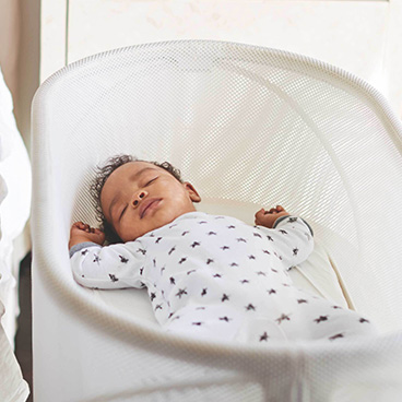 Baby sleeping peacefully in a white bassinet.