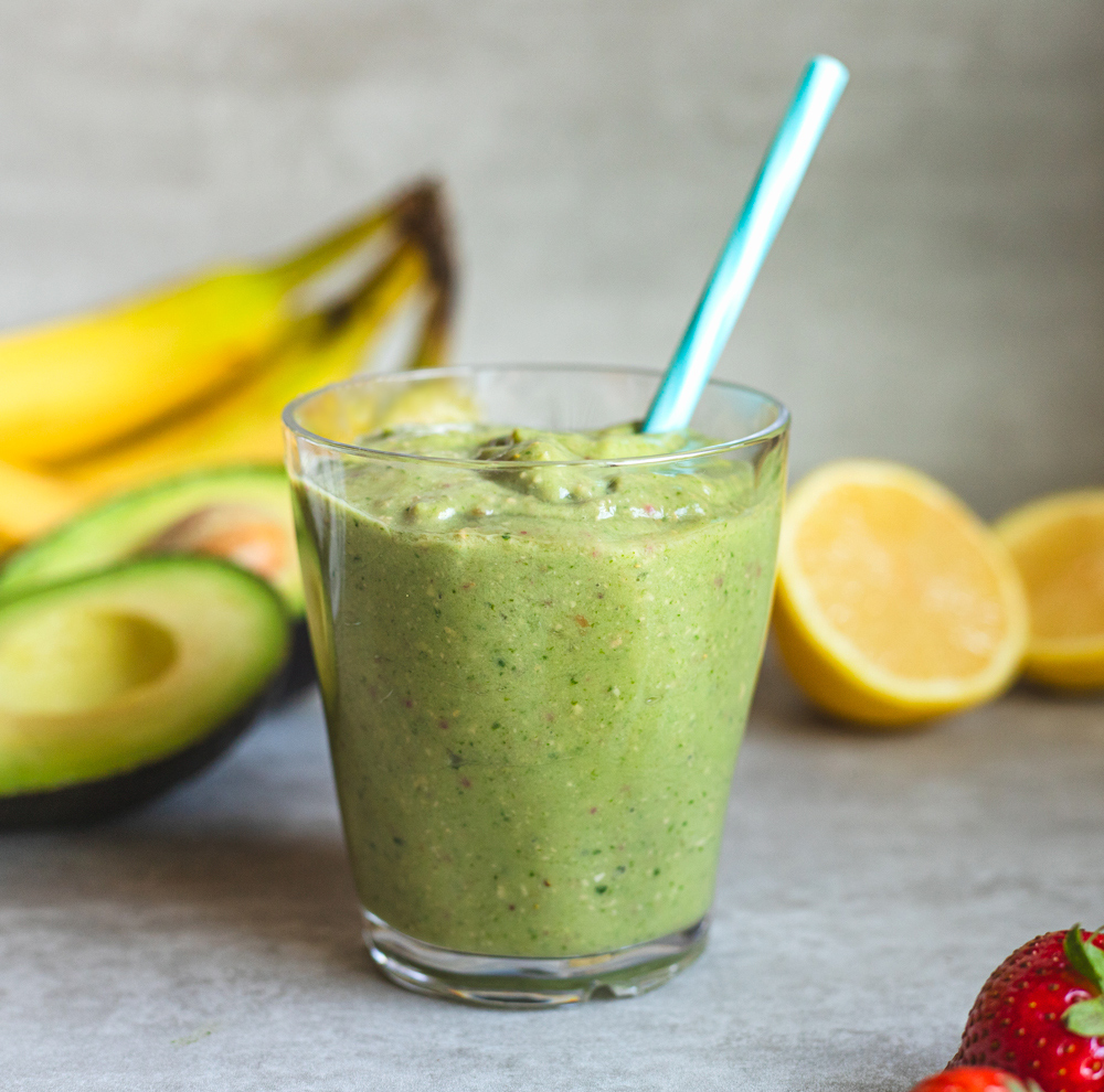 Green smoothie in glass with diverse fruits around.