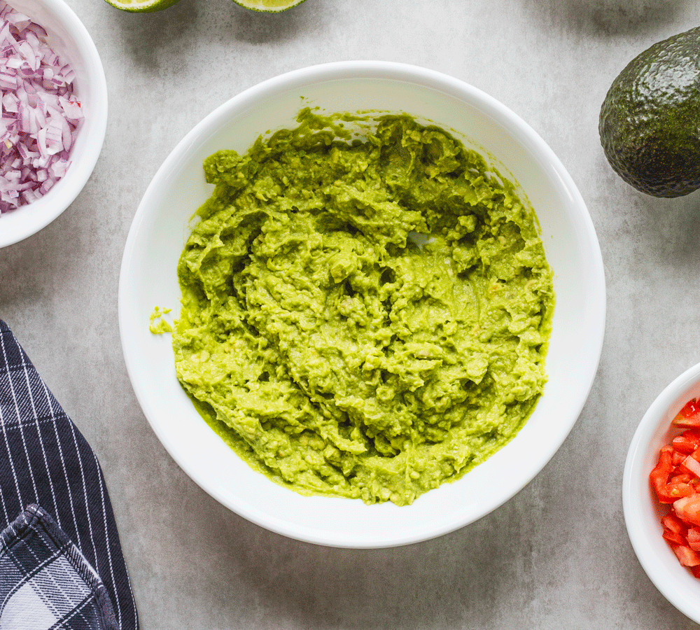 Guacamole in a bowl surrounded by fresh ingredients.