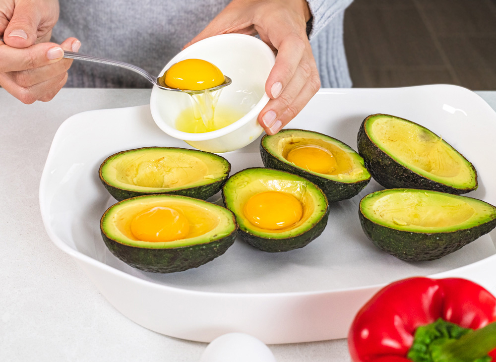Placing egg yolk into avocado half for baking.