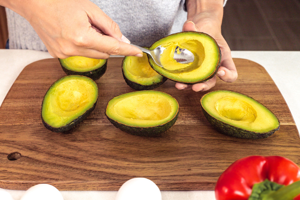 Person scooping avocados on wooden cutting board.