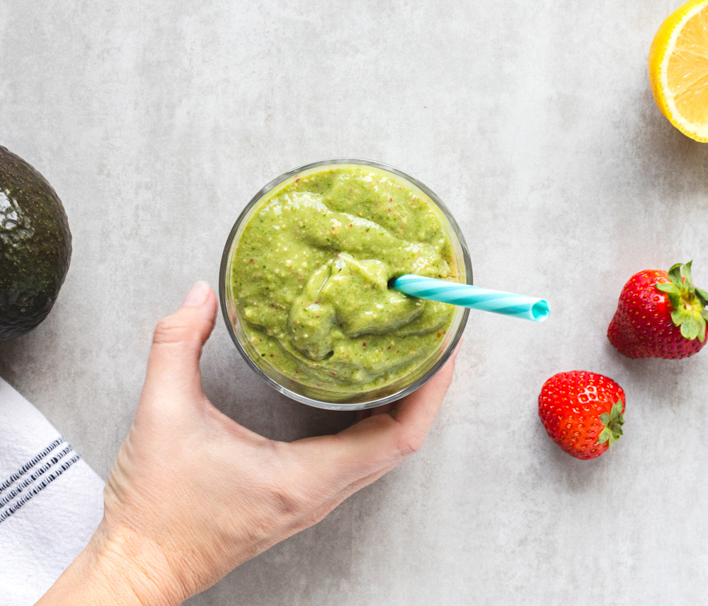 Hand holding a green smoothie with blue straw.