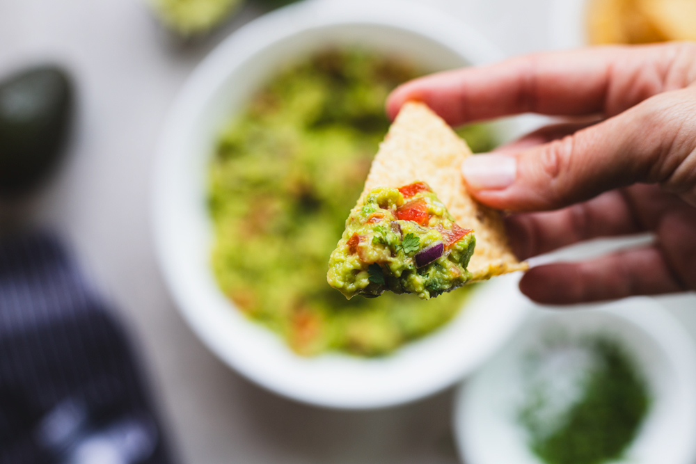 Hand holding chip with guacamole scoop.