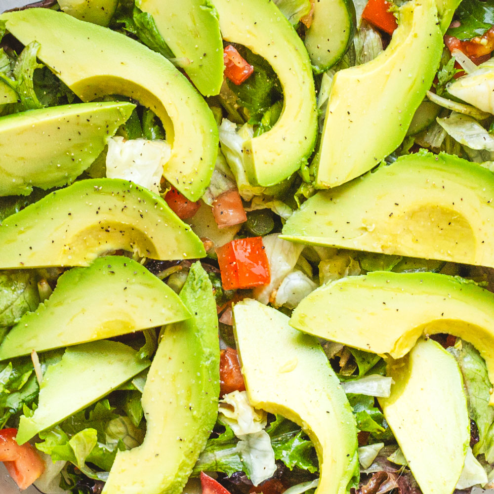 Avocado slices atop fresh salad greens and vegetables.